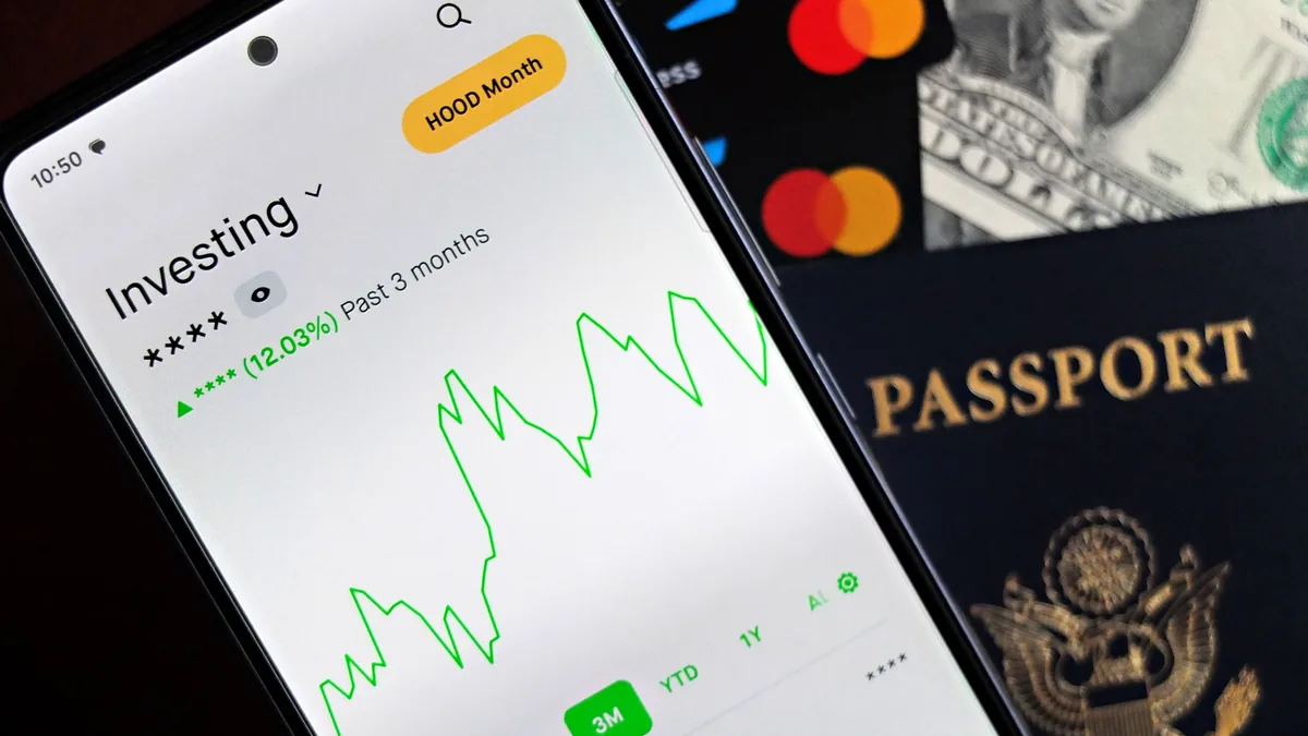 A smartphone displaying an investment app, with a passport and credit card in the background.