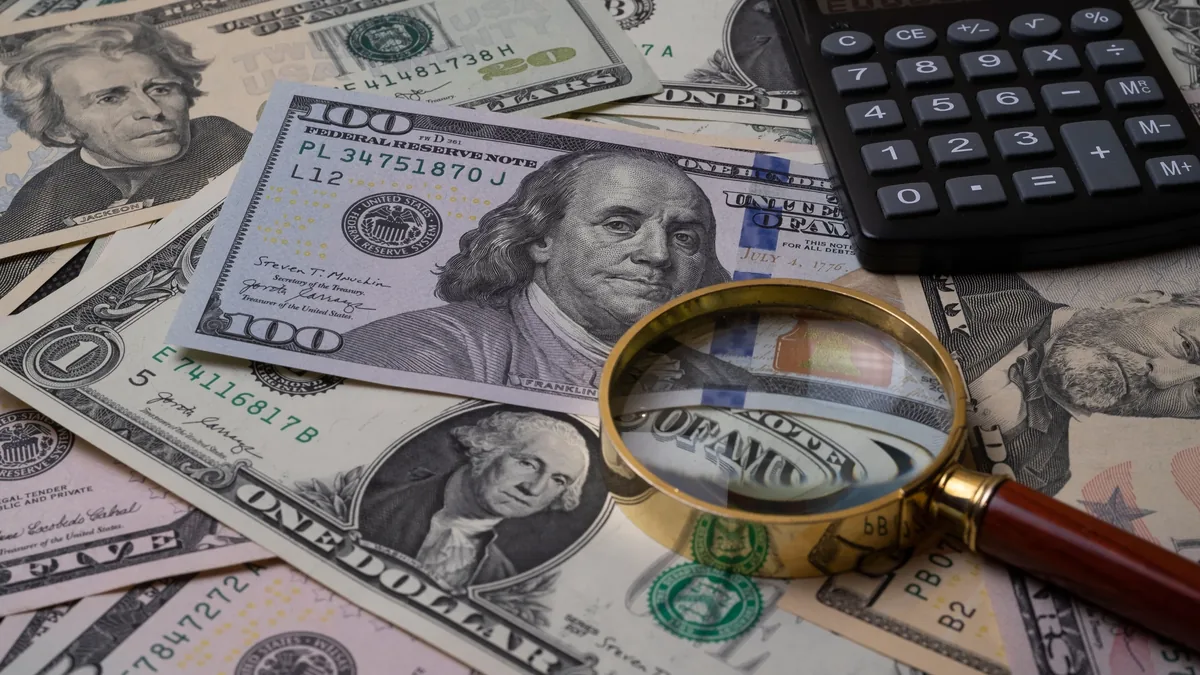 A magnifying glass, a calculator, and a collection of US dollar bills.